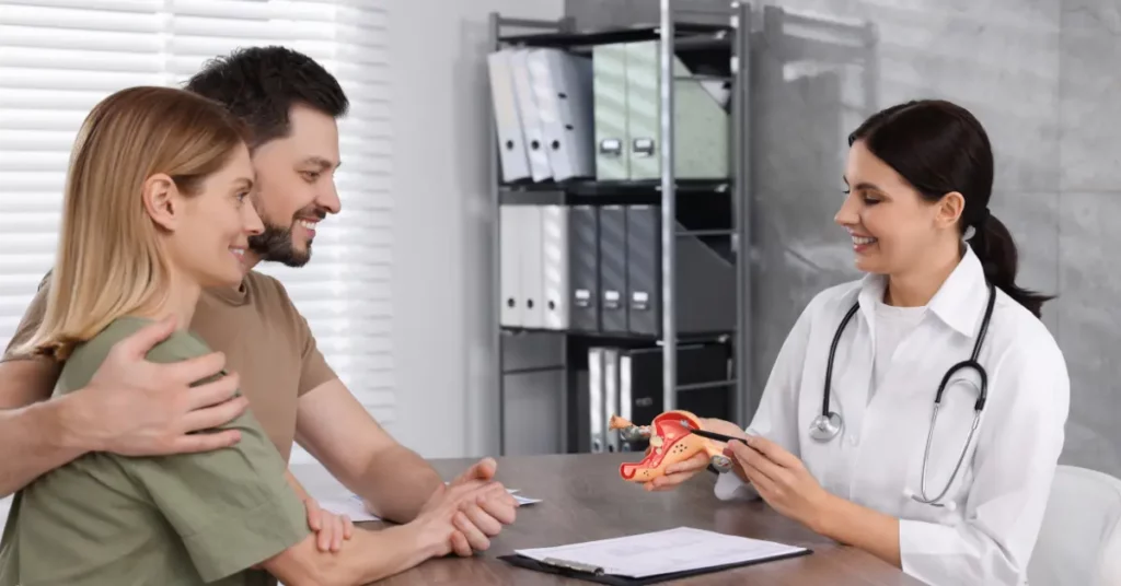 IVF consultation with a doctor showing a uterus model to a smiling couple in a clinic