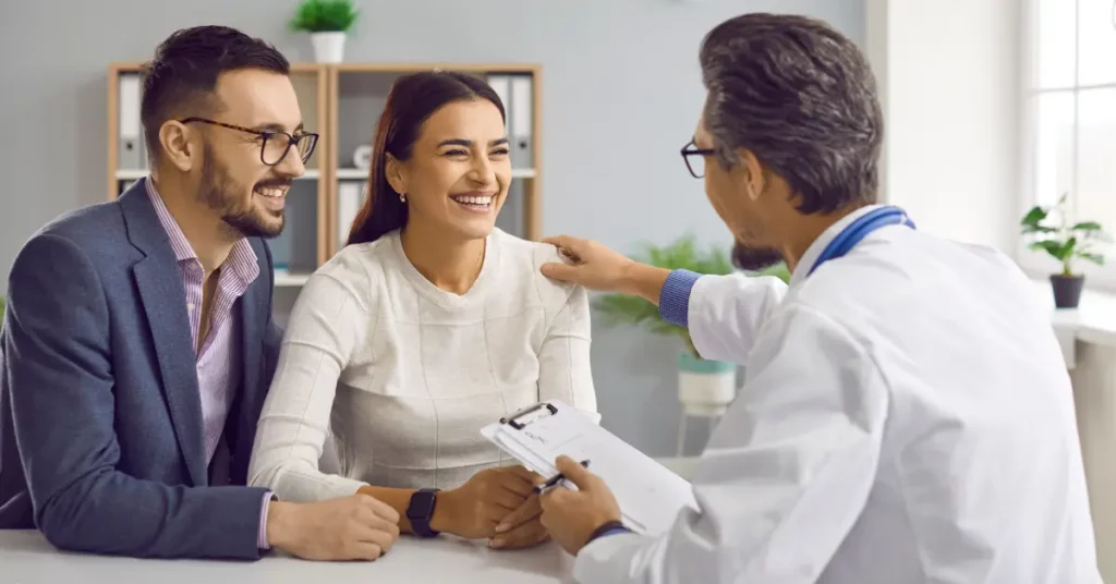 Male fertility treatments discussed between happy couple and doctor during consultation in a modern medical office.