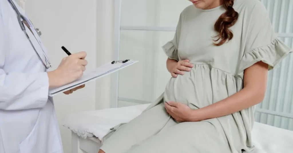 IVF fertility consultation showing pregnant woman holding belly while doctor writes on clipboard.