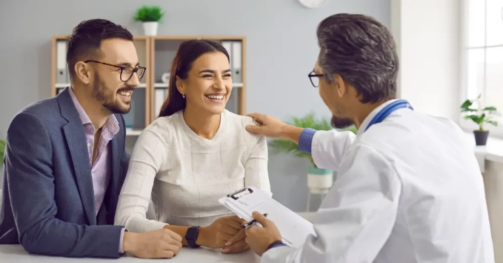 IVF fertility treatment consultation with smiling couple talking to male doctor in modern office.