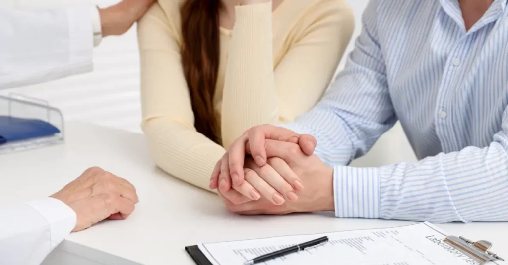 Fertility decline in men and women illustrated by a couple holding hands during a supportive conversation with a doctor.