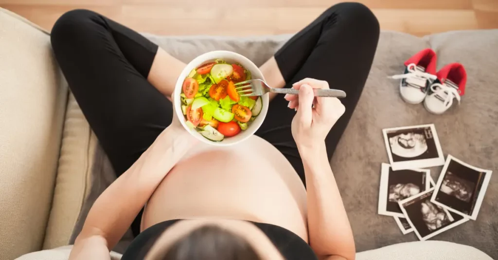 Foods for fertility shown in a bowl of fresh salad held by a pregnant woman sitting on a couch.